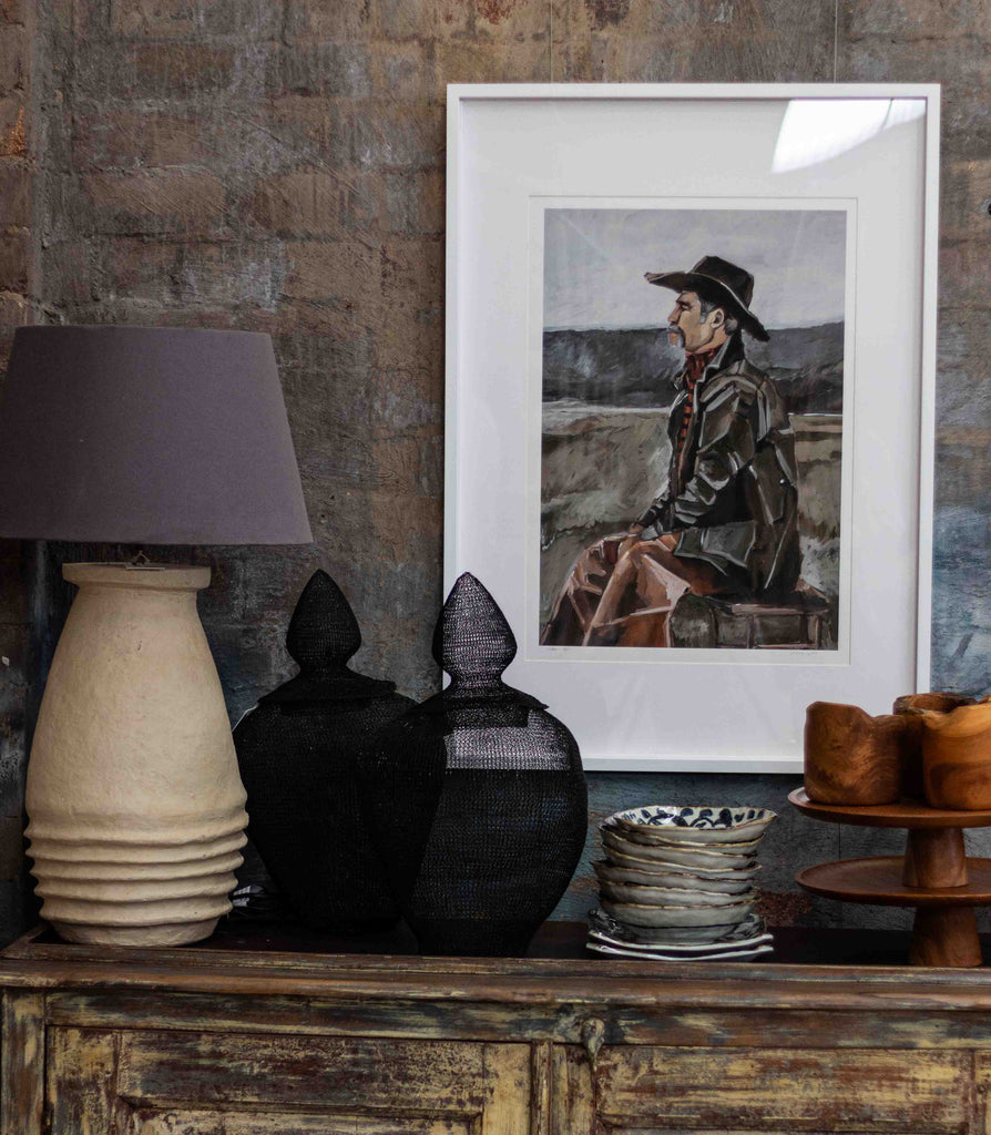 Decorative setting with a lamp, black cat figurines, framed picture, and wooden cabinet.