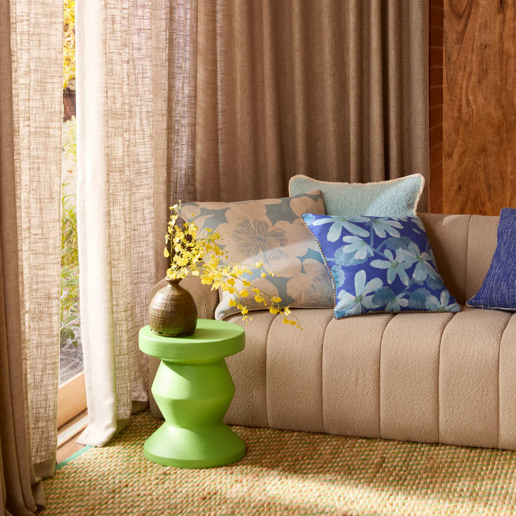 Beige sofa with floral cushions next to a green side table and curtains