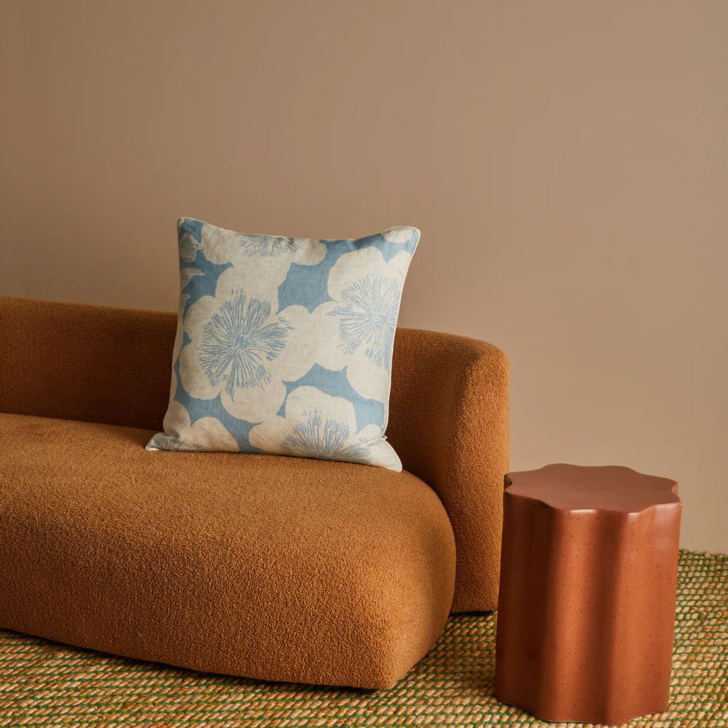 Brown sofa with a floral-patterned pillow and matching side table against a beige wall.