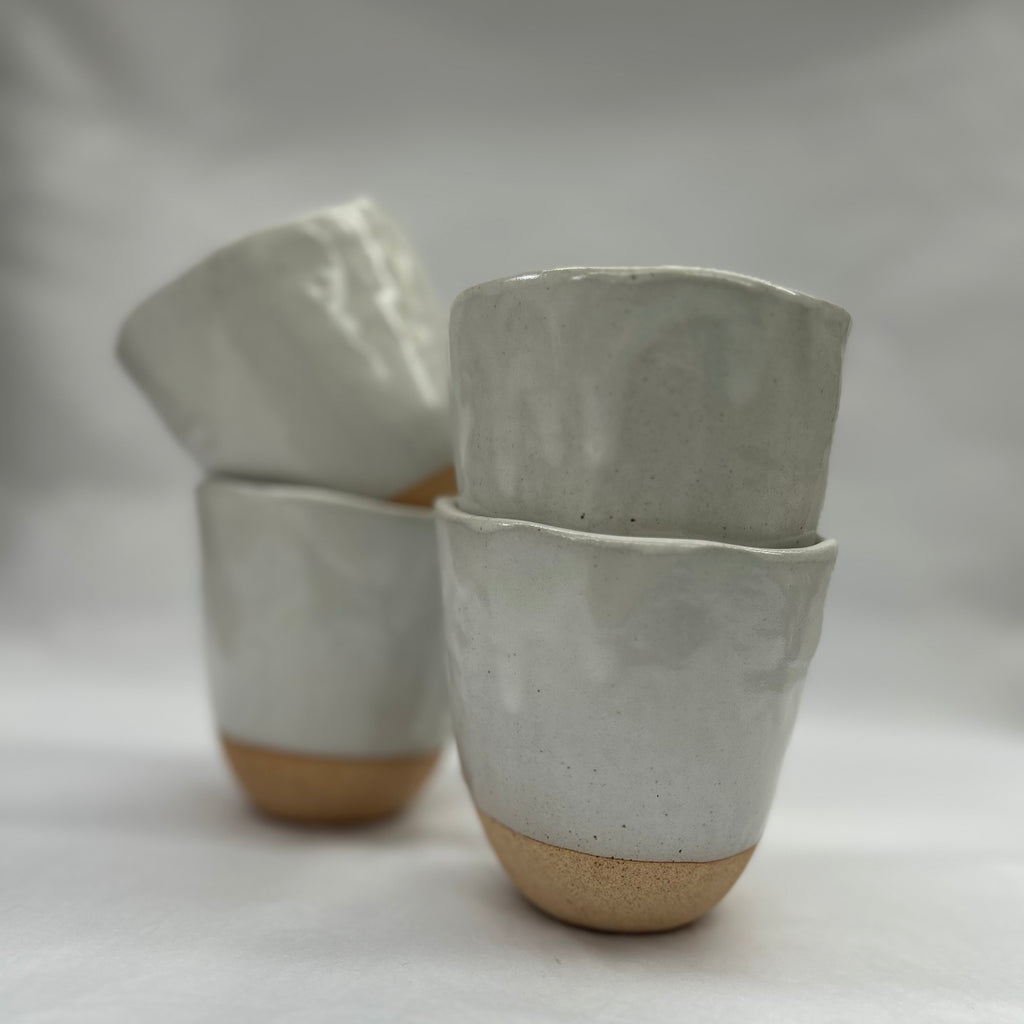 Set of four ceramic cups with a natural base color on a plain background